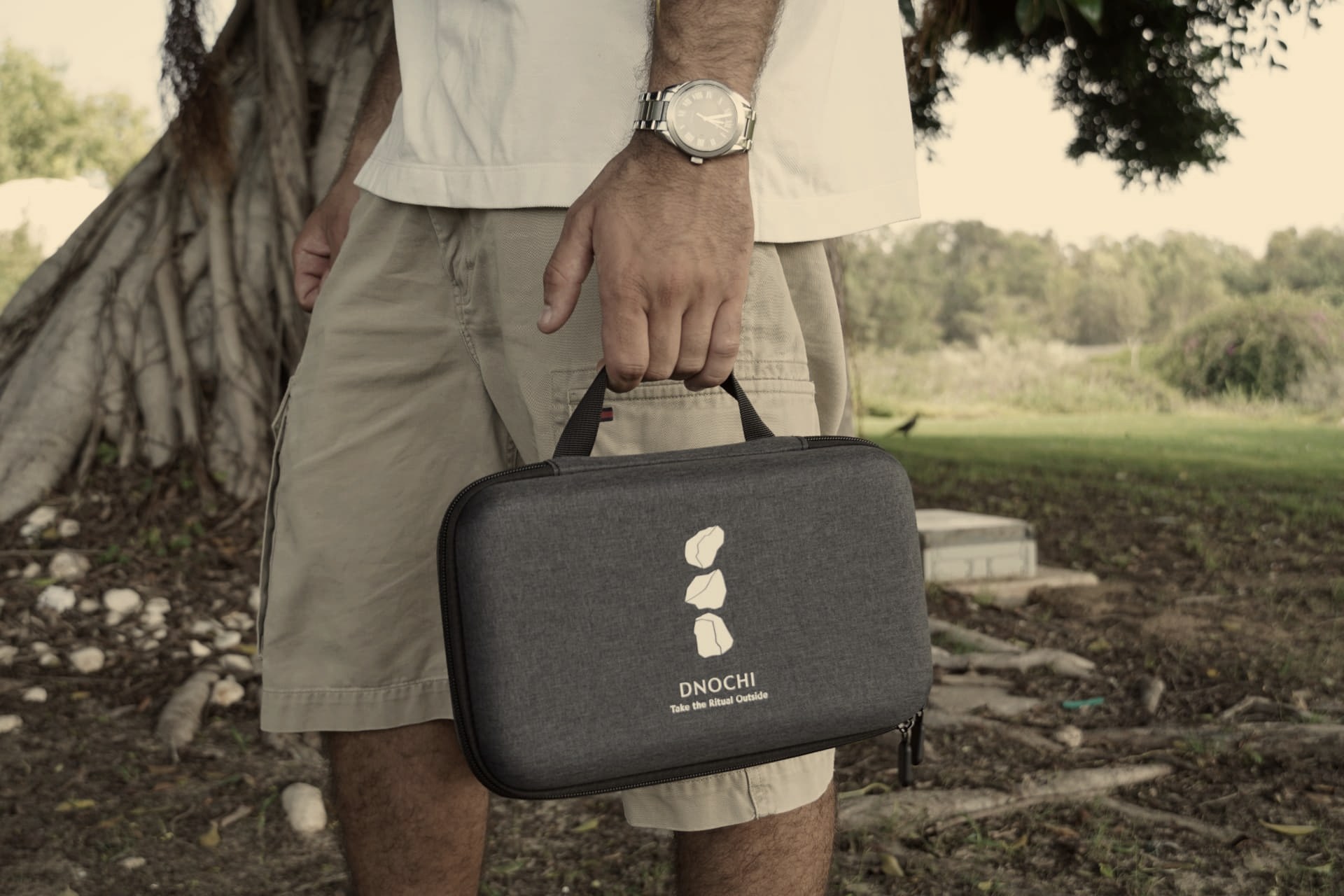 A traveller carrying the DNOCHI case through a park at midday